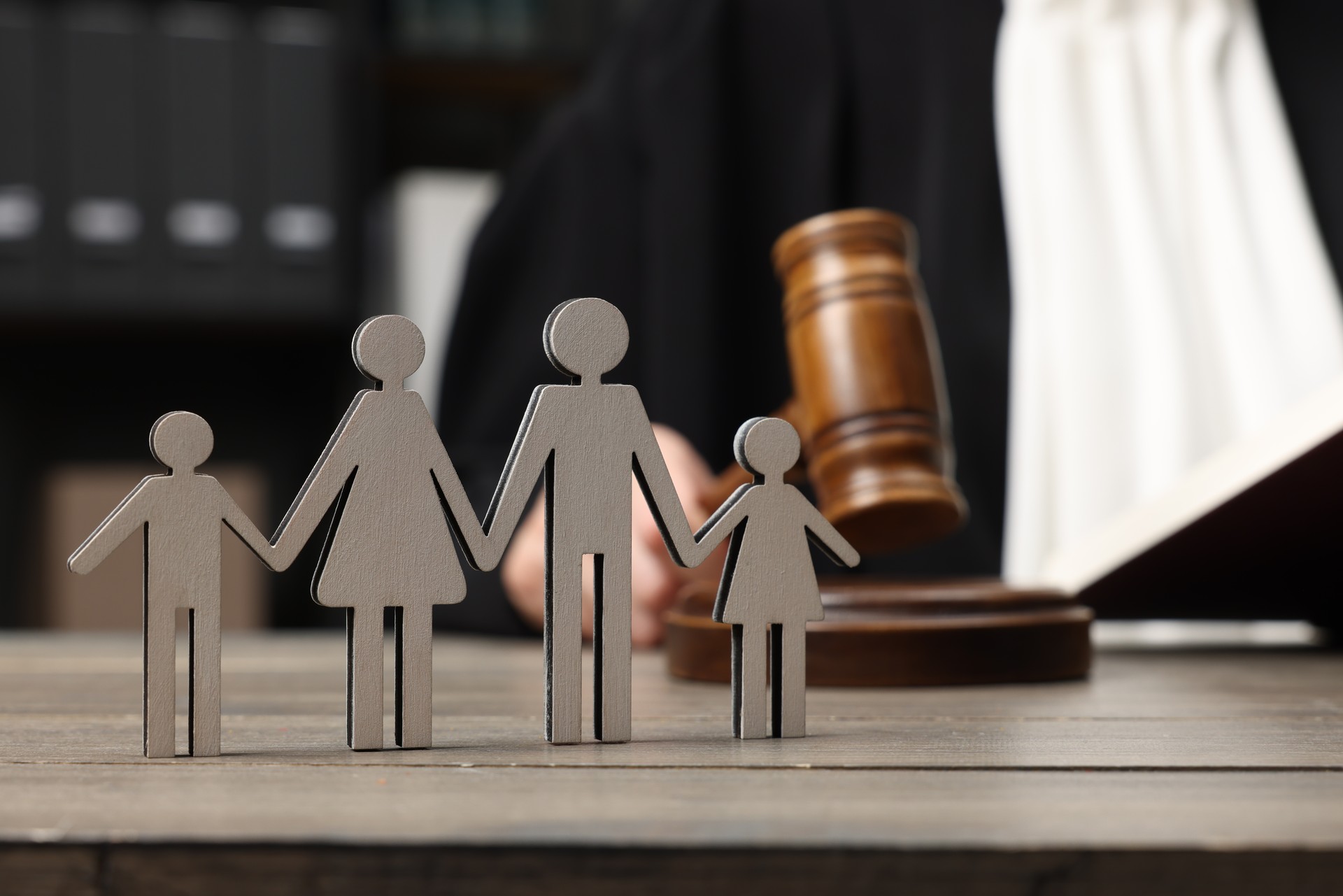 Family law. Judge with gavel sitting at wooden table, focus on figure of parents and children