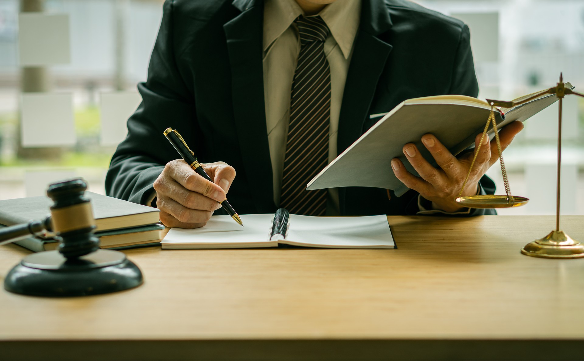 Judge's hammer and golden scales and a courtroom lawyer on a wooden table and a male counselor or lawyer working in the office. Law, advice and justice concepts.